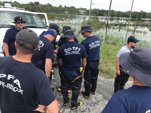 Search and rescue members in dark blue uniforms huddle in a group to prepare for rescues.