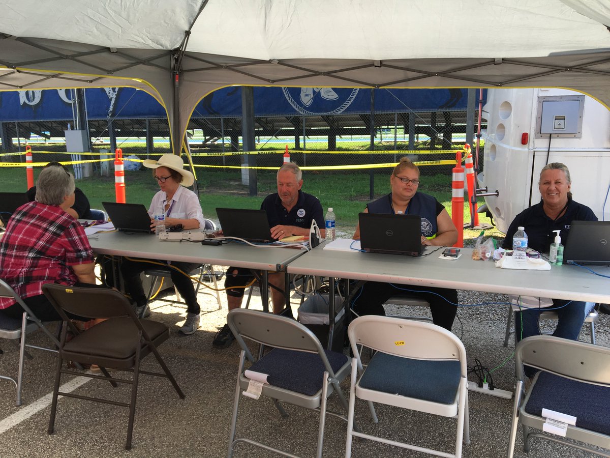 A group of FEMA employees sit at laptops at a long table under a tent.