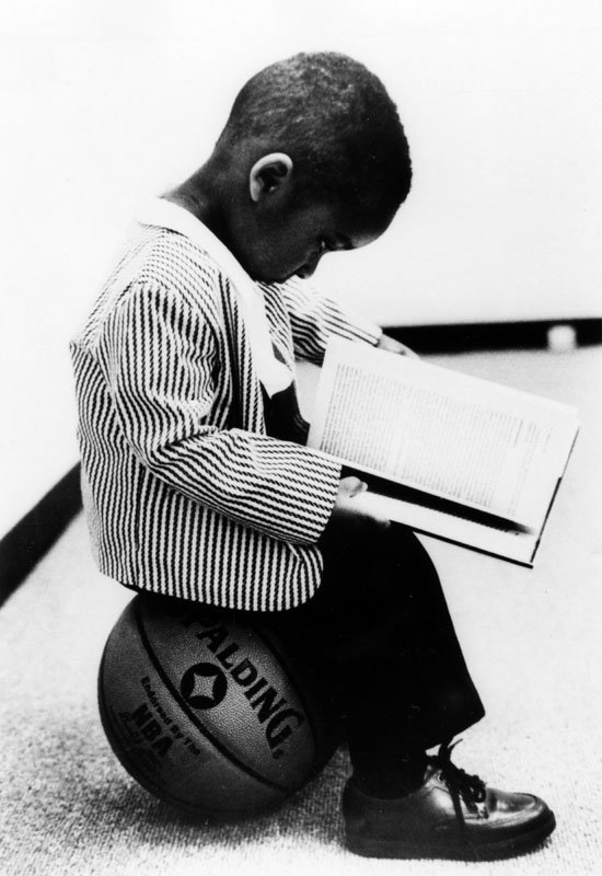 Boy reading a book sitting on a basketball