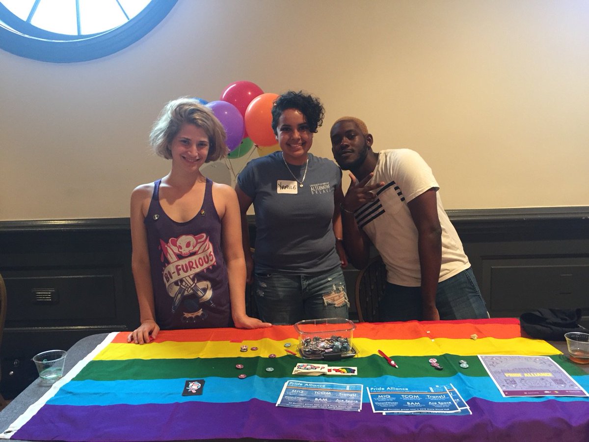 Left to right: Savannah (they/them or she/her), Yamile (she/her), Aaron (he/him) behind a table representing the Pride Alliance.