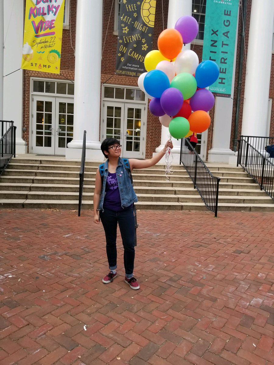 Max (he/him) holding rainbow color balloons.