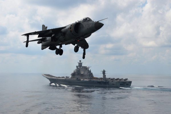 A picture that tells a whole story. Sea Harrier on final flight as Vikramaditya, laden with MiG-29Ks, sails into view!