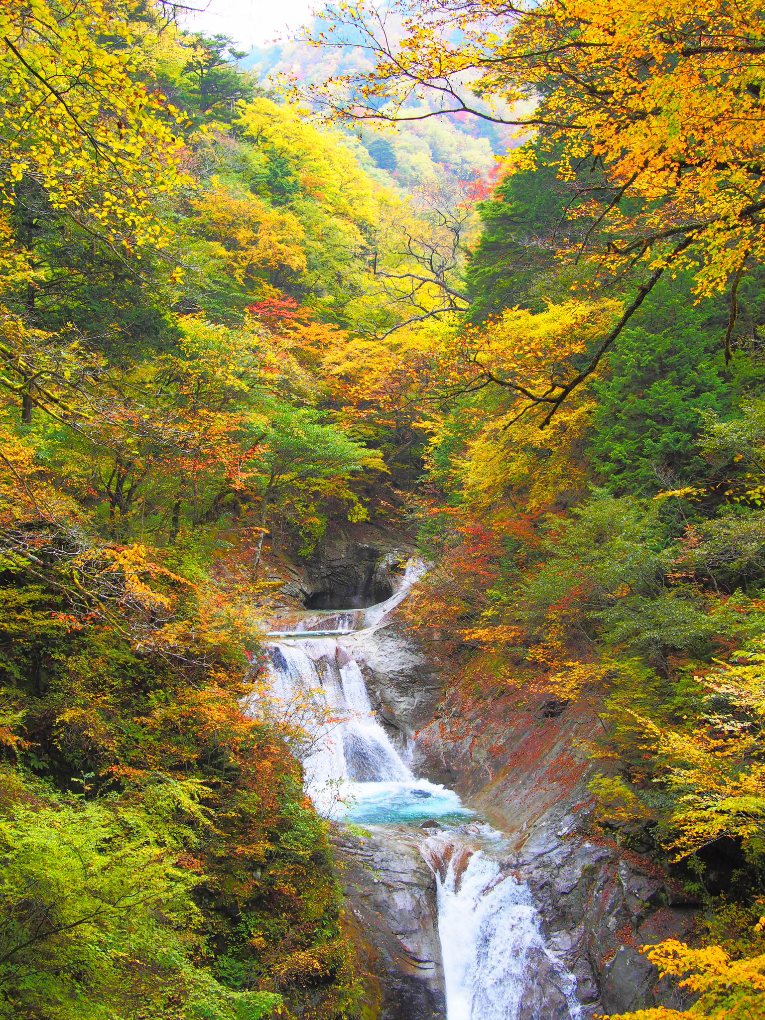 山梨市観光協会 西沢渓谷の紅葉 今年は10月日ごろから見ごろとなる予想のため まだ紅葉には少し早いです 写真は過去のものですが 七ツ釜五段の滝の紅葉です 向こうに見える山も含めて