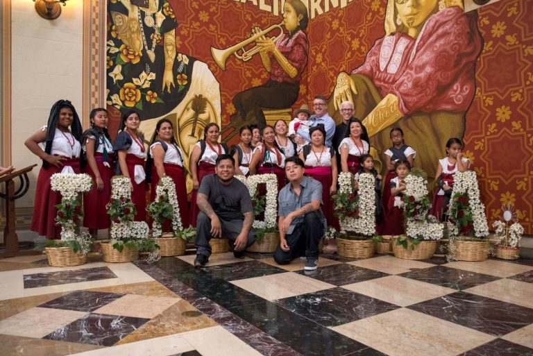 Artists and band stand in front of Visualizing Language mural