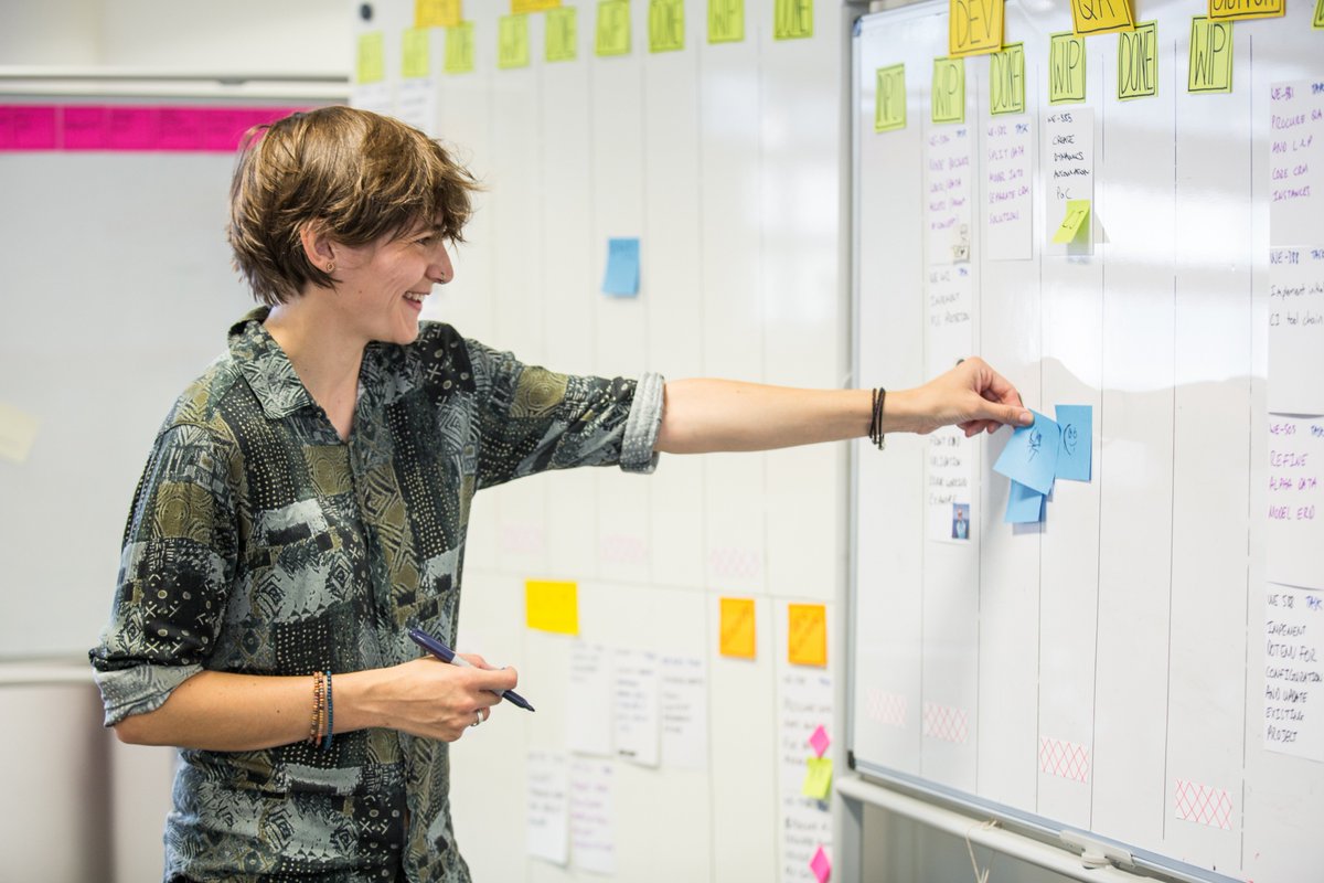 Photo of young woman smiling adding post it to white board