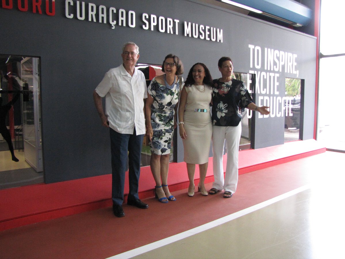 Enith Brigitha en Jeannette van Ditzhuijzen bieden een exemplaar van het  boek aan Minister van Sport op Curaçao Marilyn Alcalá-Wallé en worden  ontvangen door de directrice van de nationale bibliotheek Gerda Willems.