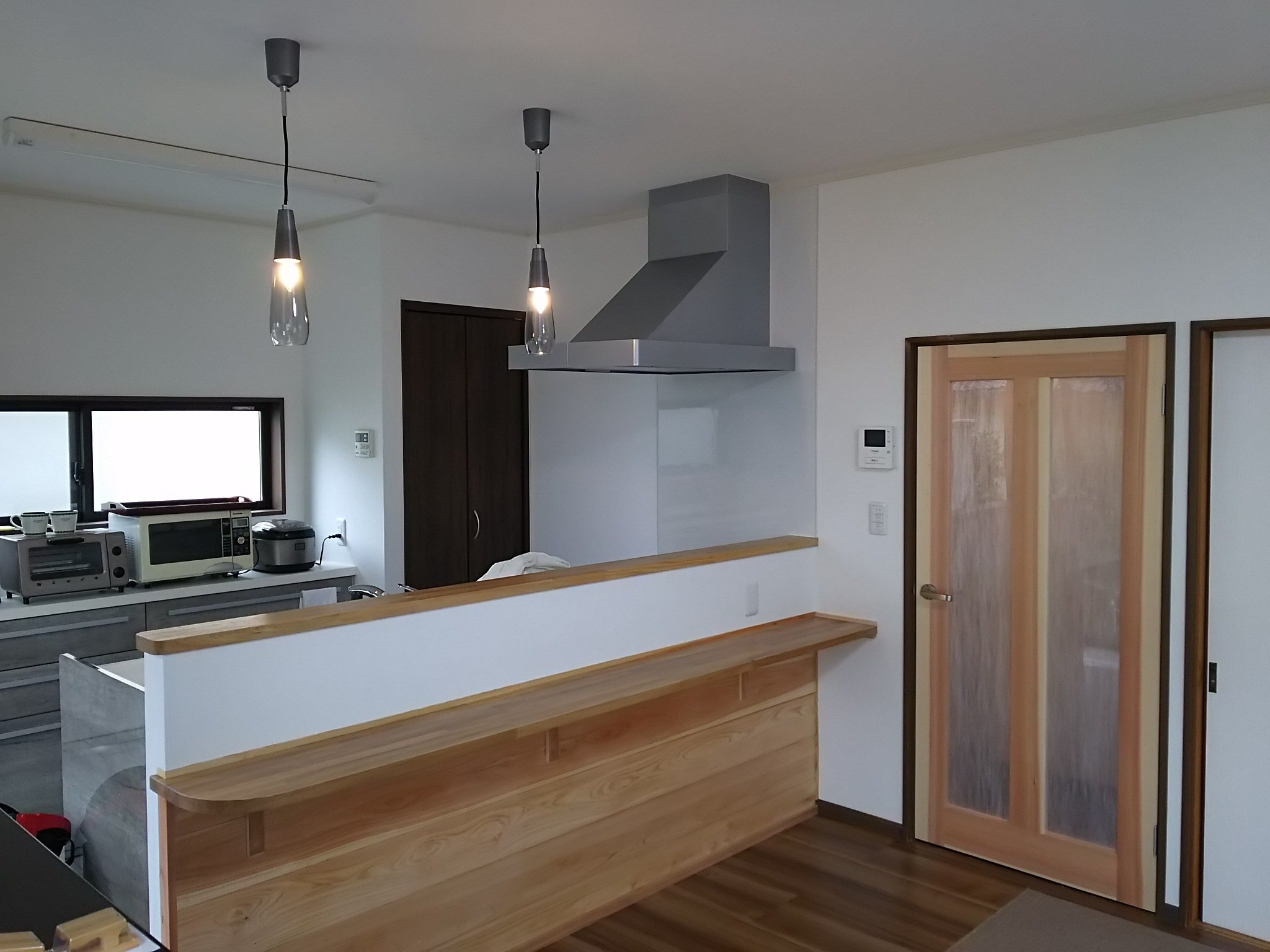 トージロー建築工匠 ひとつのｌｄｋですが 対面キッチンを境に リビングスペースを木目の床板に キッチンスペースを石目調の床板にと雰囲気を変えてみました キッチンの手元とカウンターを照らすブラケットライトは安くてお洒落なエルックスの照明