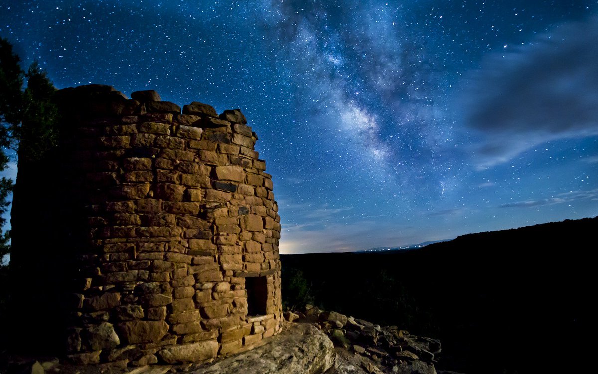 The remains of an old stone building stands on a desert plain under the night sky.