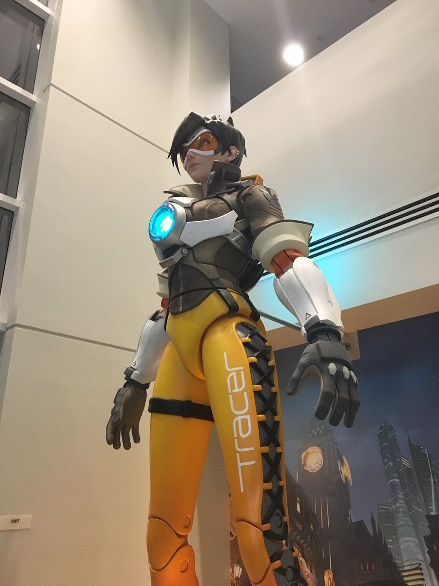a giant statue of Tracer from Overwatch designed to look like a pose-able action figure. The chronal accelerator in the middle of her chest is lit up in blue.