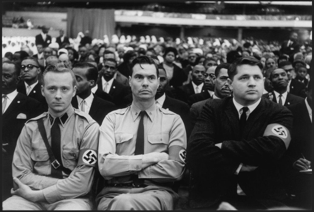 Impressionante fotografia mostra o líder do Partido Nazista Americano, George Lincoln Rockwell, ao lado de dois assistentes, assistindo a uma fala do líder negro Malcolm X, durante a reunião de cúpula da Nação do Islã, em 1961.