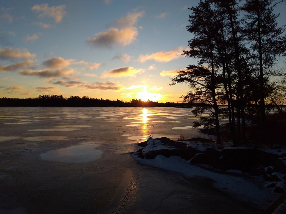 A golden sunrise over a frozen lake bordered with trees and snow.