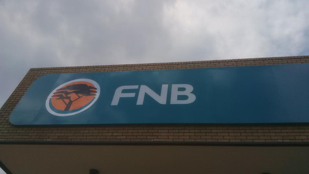 SAMMNewsGraphic's tweet photo. A word-mark and logo of the First National Bank super-placed on the edge of the part of the bank's building upwards https://t.co/Iypzzp8Fxl