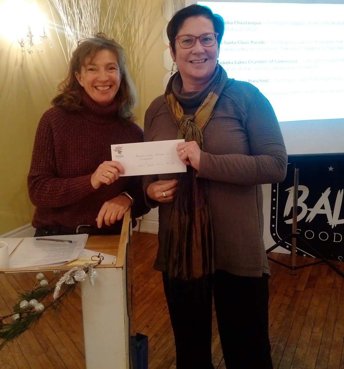 MuskokaLakesCC's tweet photo. Thank you @BalaCranberry for including the Chamber in your grants given out tonight: Chamber Treasurer Sheila Overbeek accepts cheque from Festival President Tiffany Bol for Bala Santa Claus Parade https://t.co/wvbPouTQEc