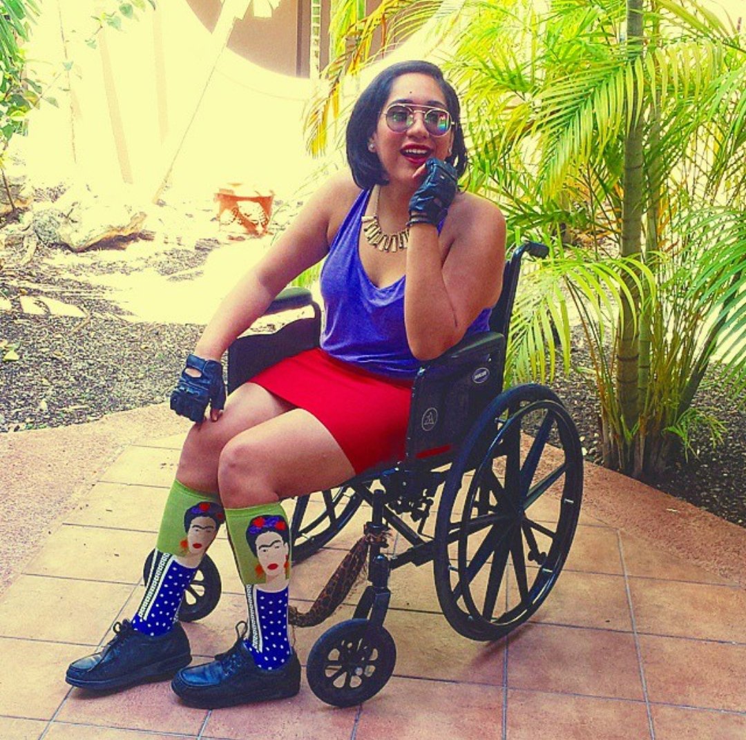 [Annie outdoors sitting in a black manual wheelchair wearing a purple top, red skirt, and Frida Kahlo socks]