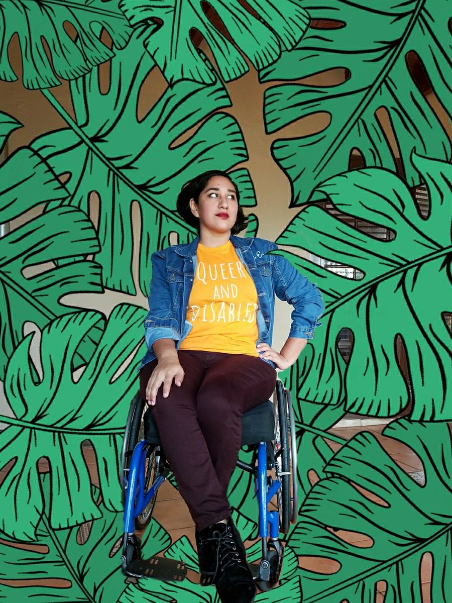 an altered photo of Annie surrounded by green leaves sitting in a blue manual wheelchair wearing an orange "Queer and disabled" shirt