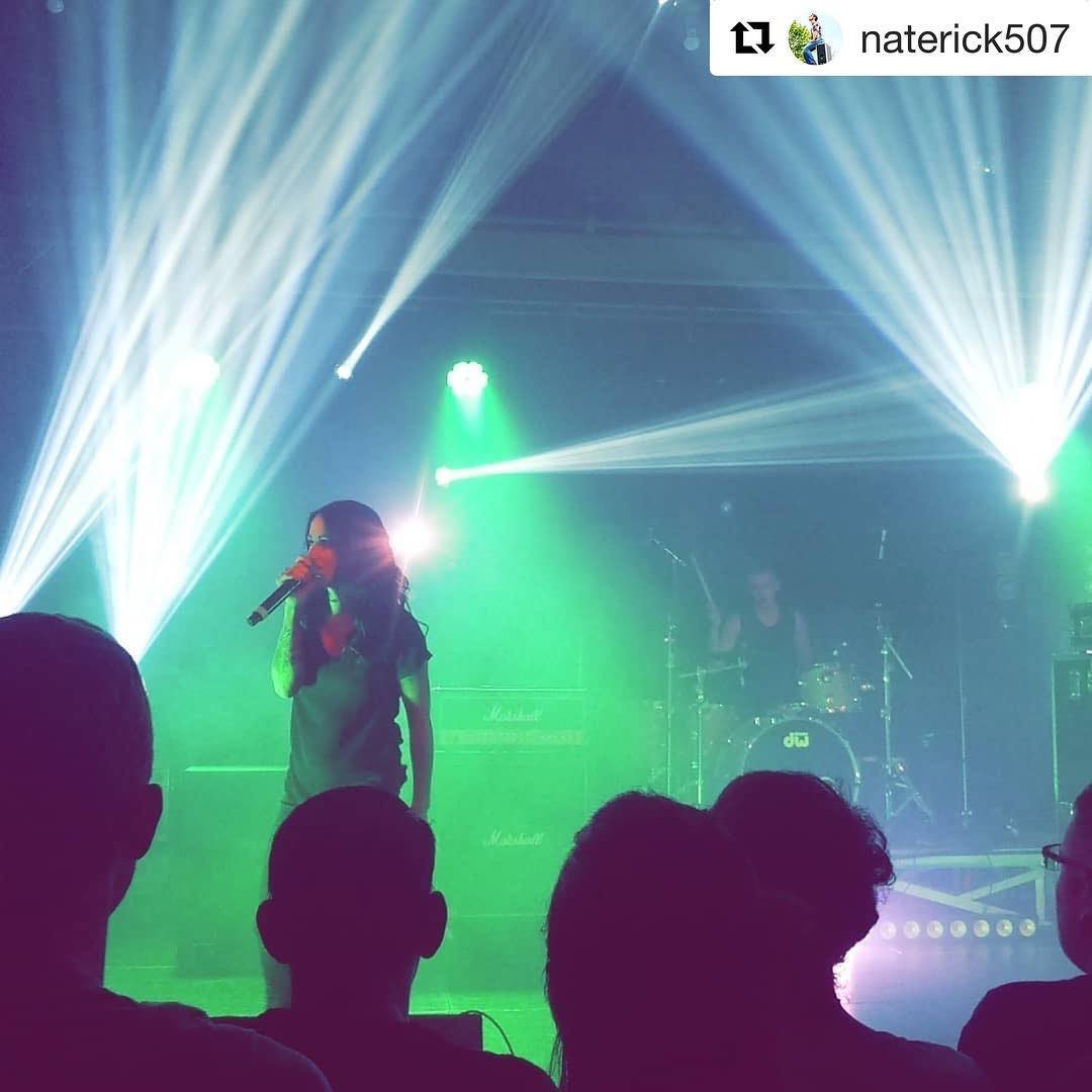 Lead singer for the Letter Black looks out to the crowd at Christmas Rock Night. She is holding a microphone to her mouth, while green and blue lights are behind her.