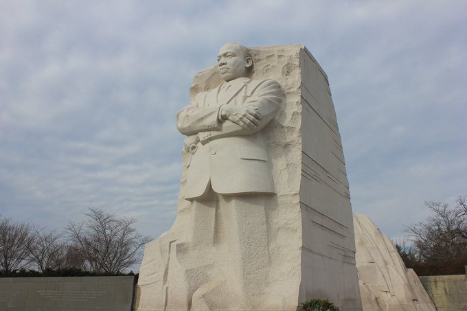 Large white granite statue of Martin Luther King Jr. in front of a cloudy sky on the National Mall in Washington, DC.