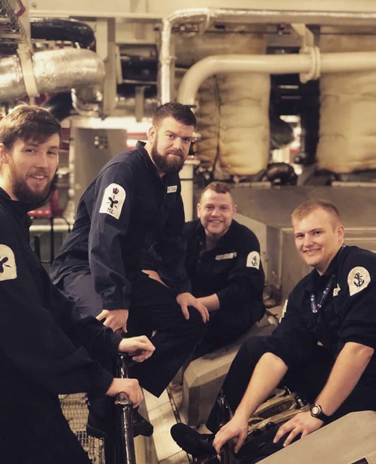 Four Marine Engineers sit atop of a wartsila engine. They are seen conducting a rocker arm change.