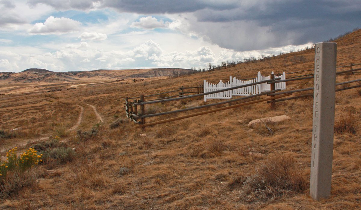 A cement marker says Cherokee Trail and a small white fence marks a grave marker behind.