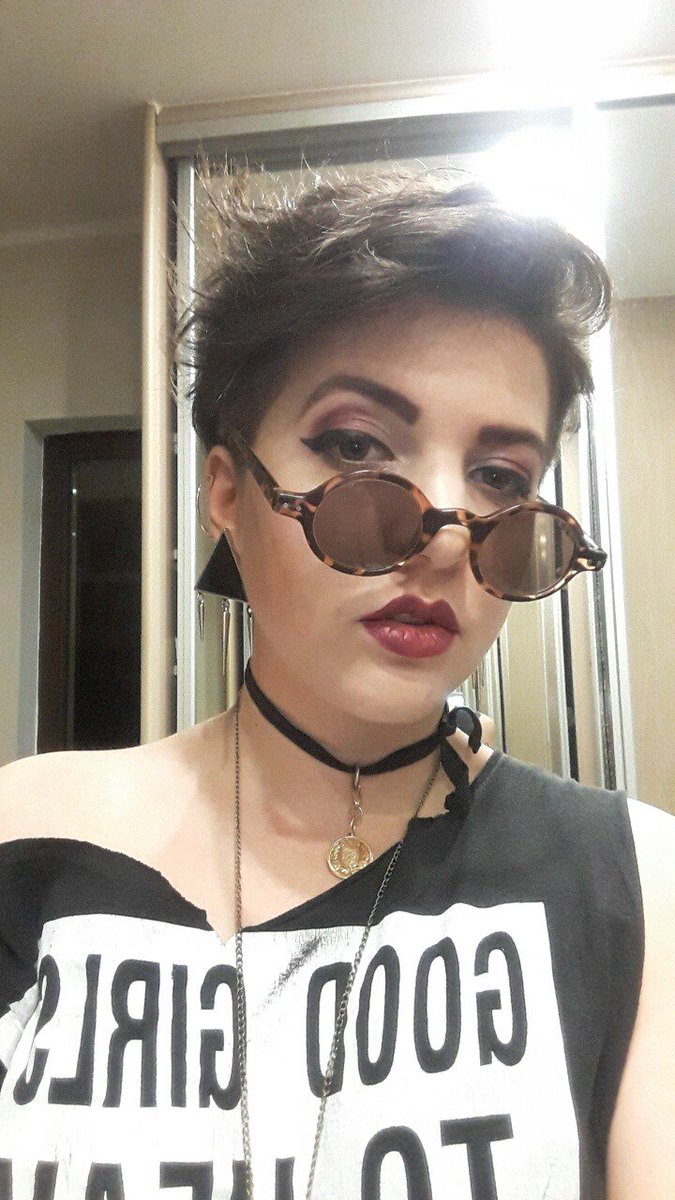 portrait picture of me, a young white woman with short brown hair, black and gold jewelry, round sunglasses, and strong purple makeup