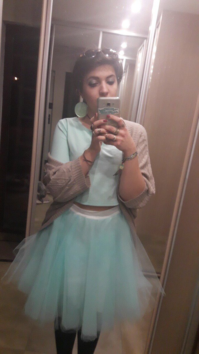 a full body picture of me, a young white woman with short brown hair, light blue makeup, and wearing a turquoise fluffy skirt, crop top and large earrings, along with a drooping brown sweater
