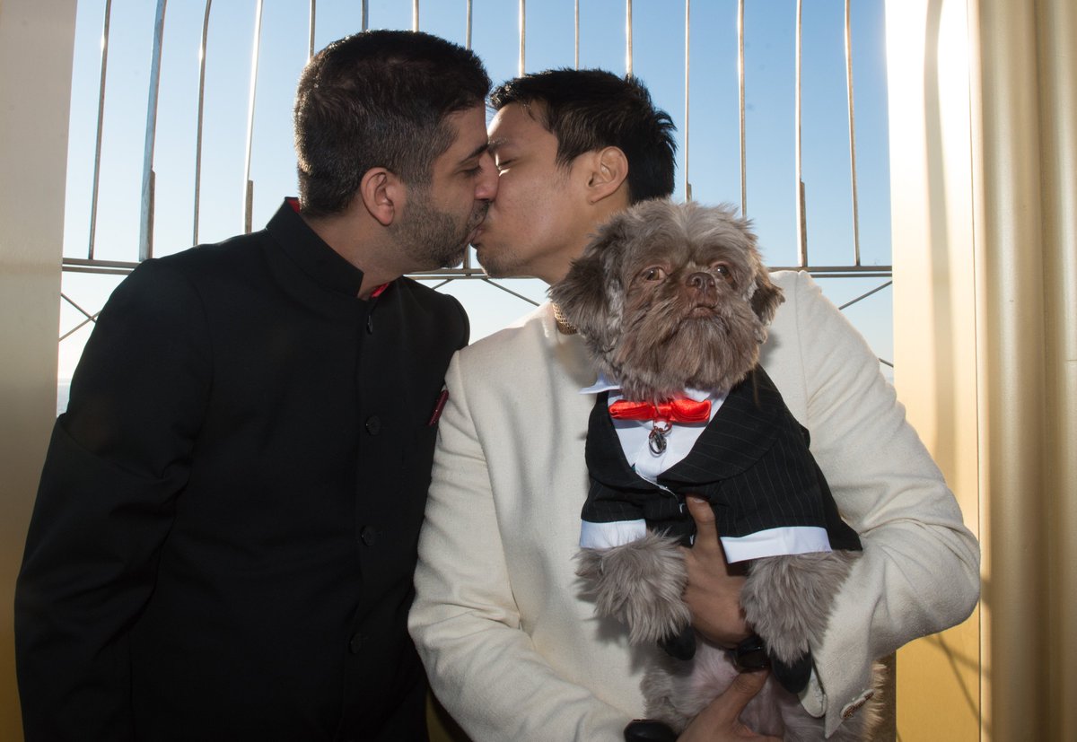 EmpireStateBldg's tweet photo. From a dating app to the top of the #EmpireStateBuilding, Hector &amp; Vijay were one of the lucky couples that renewed their vows atop our tower in 2016! Joining them in the ceremony was their dog @KokiStateOfMind who dressed up for the ocassion! #ESBeMine https://t.co/MhzktxcVHt