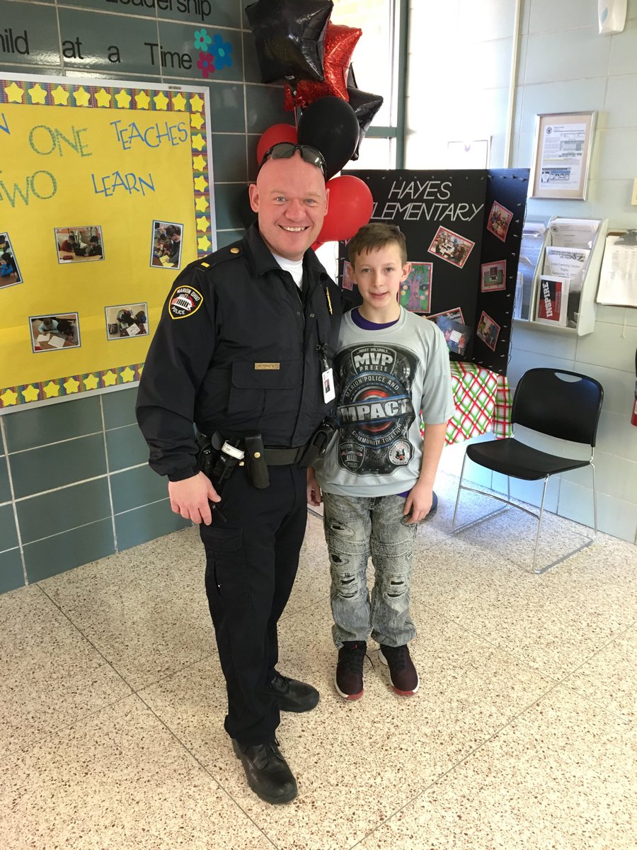 A fourth-grade student receives the impact award and  personalized T-shirt from the school resource officer.