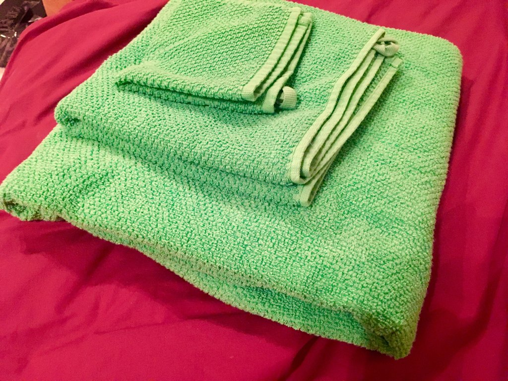 A green flannel, hand towel and bath towel in a pile on a red duvet