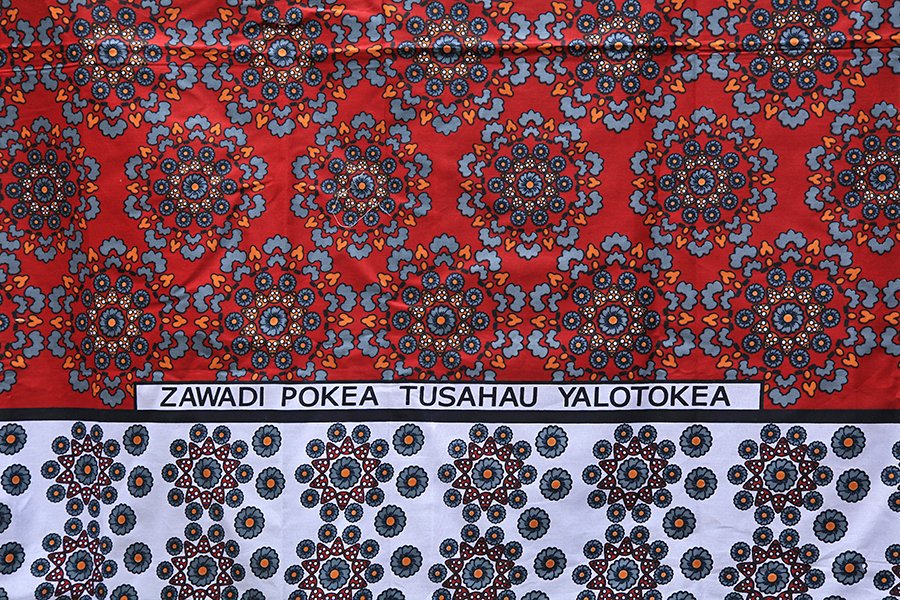 Kangas were often made in India for sale in Africa. The inscription on this kanga, written in Swahili, reads "Take this gift and let us forget what happened before". This is said to be a kanga of 'reconciliation' to be given to someone after a disagreement or as a peace offering