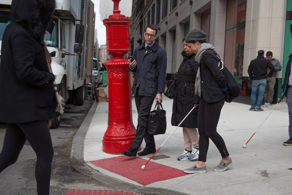 Group of three people crossing a street, two people using a cane