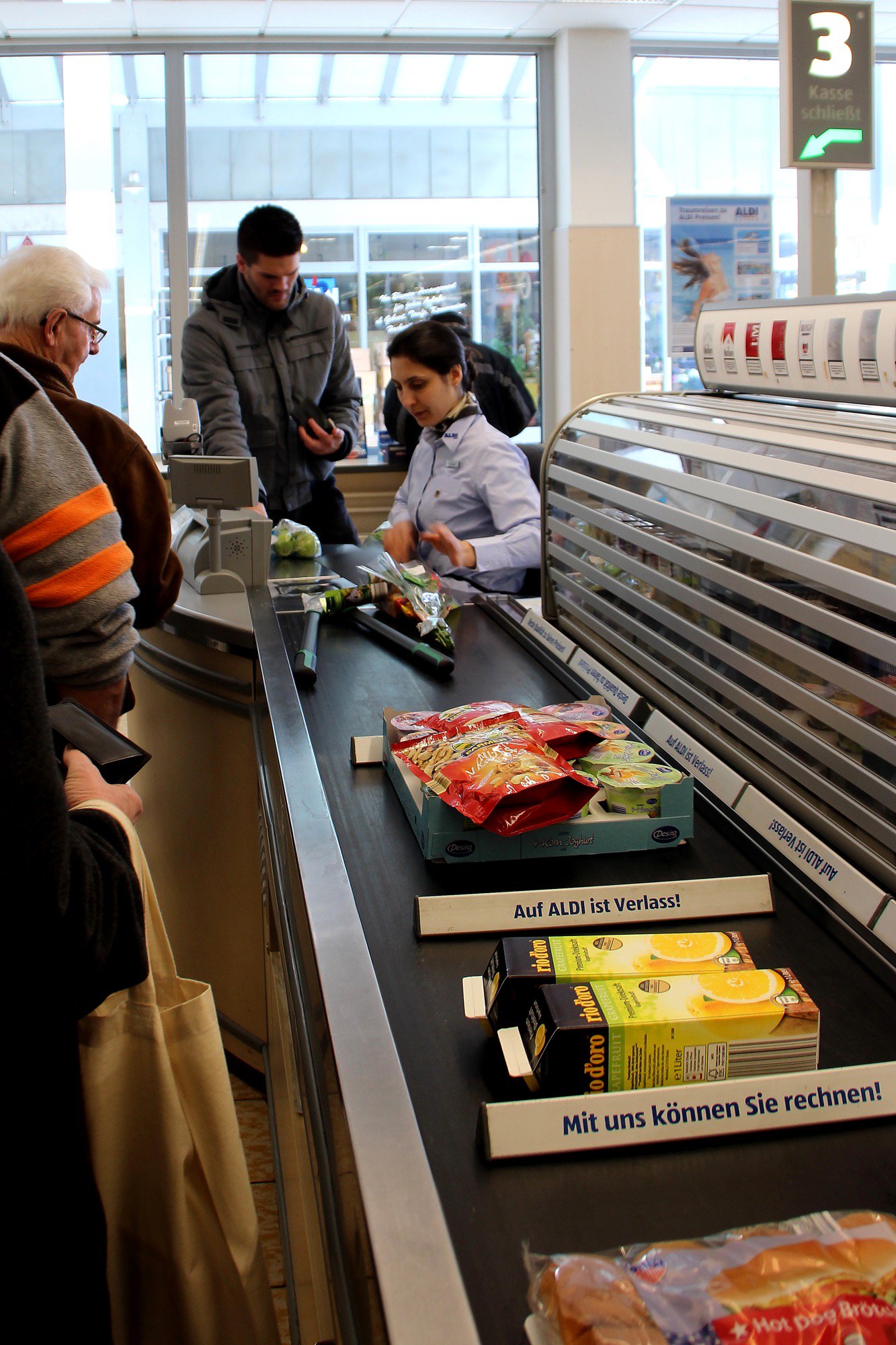 ドイツ通信 ドイツのスーパーと言えば このレジ のベルトコンベアが特徴です 自分で買った物をこのベルトコンベア上に出し 奥で座っている店員さんがバーコードを読み取ります その後は 買った物を右に流されるので レジ横で袋詰めをします 袋詰めの