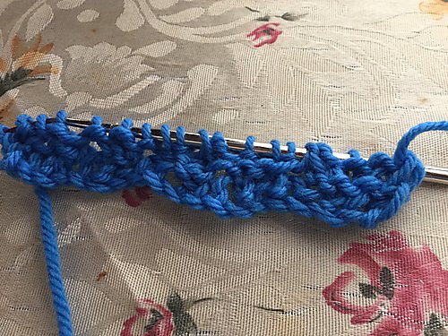 It is a simple blue tangled cord. Maybe something knitted, maybe a knot from the last chapter of the scout handbook.