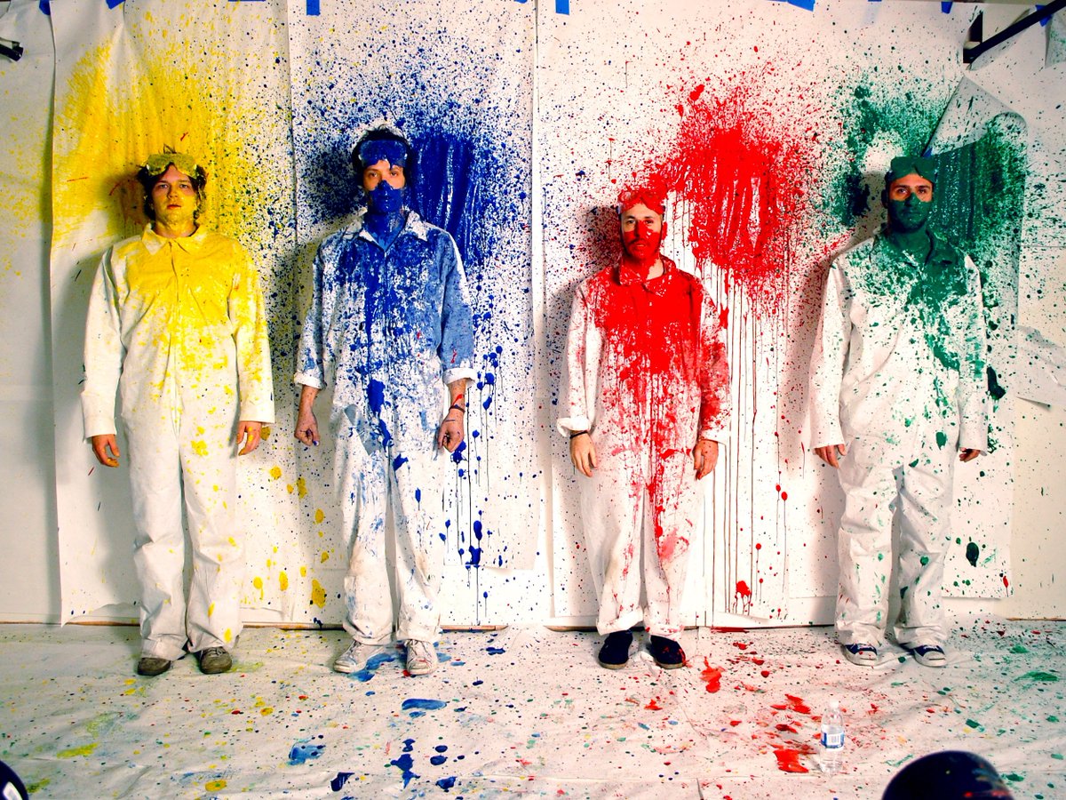 Members of the band Ok Go splattered with yellow, blue, red, and green paint, from the music video for "This Too Shall Pass"