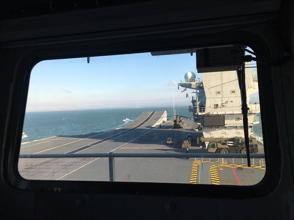 Looking down at the flight deck through a window in the aft island. The exterior of the window is silhouetted and a vertical windscreen wiper is visible.