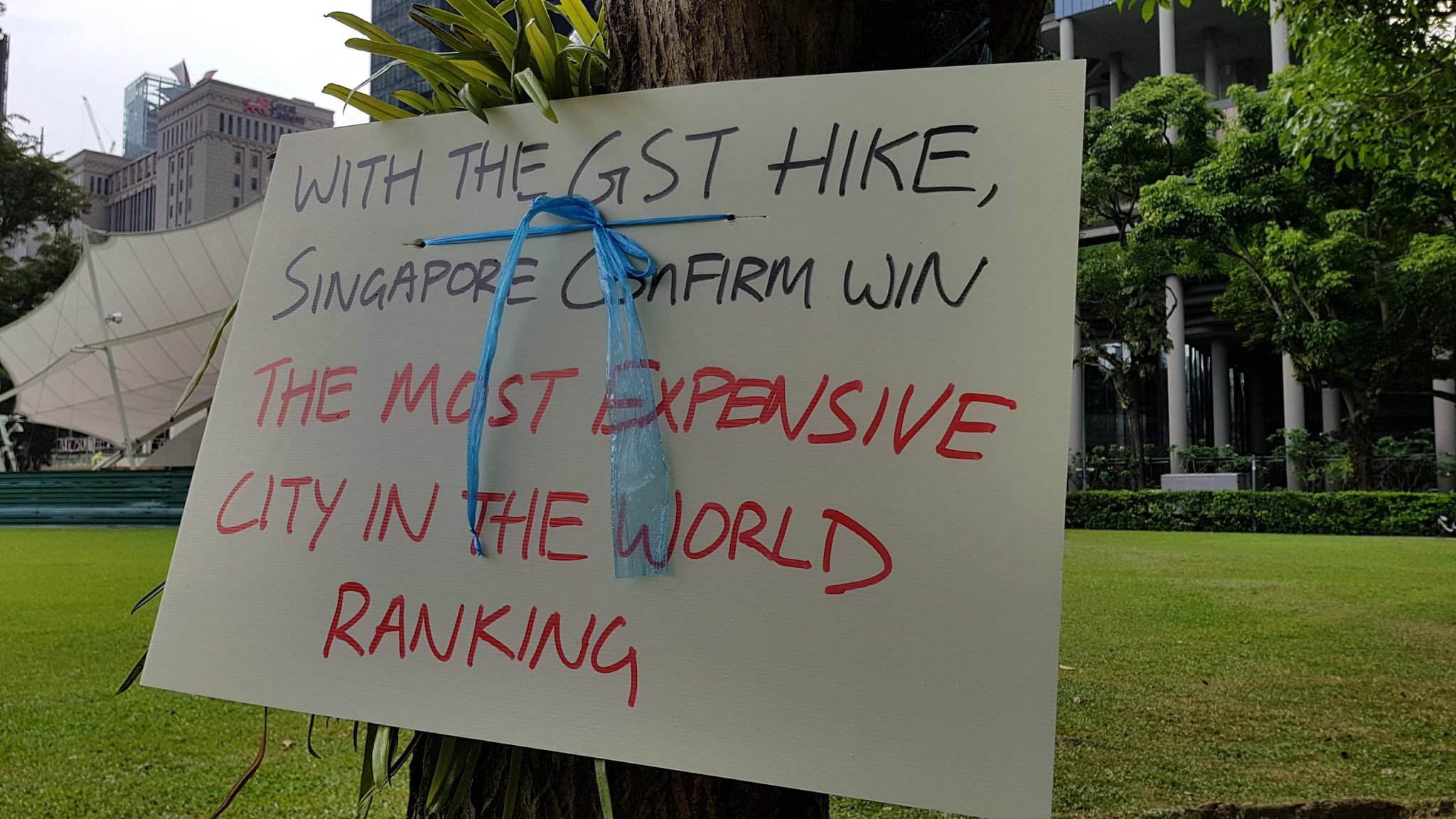 A picture of a sign from a protest against the planned GST increase. It reads "With the GST hike, Singapore confirm win the most expensive city in the world ranking"