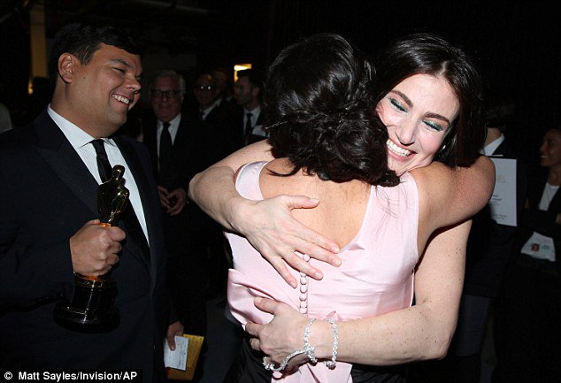 Idina Menzel hugging Kristen Anderson-Lopez after Oscar win for Let It Go as Robert Lopez smiles in the background holding the Oscar