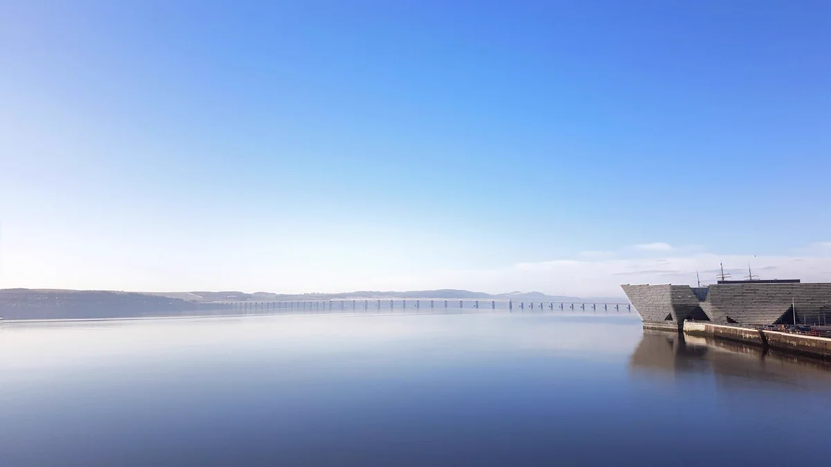river Tay with Dundee waterfront on the right. sky is clear and blue and perfectly reflected in the calm water.