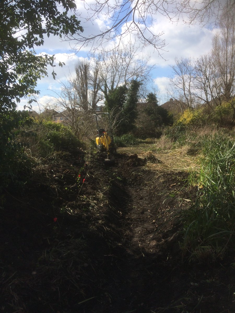 Image of  a freshly dug ditch in a field with a small digger at the end.