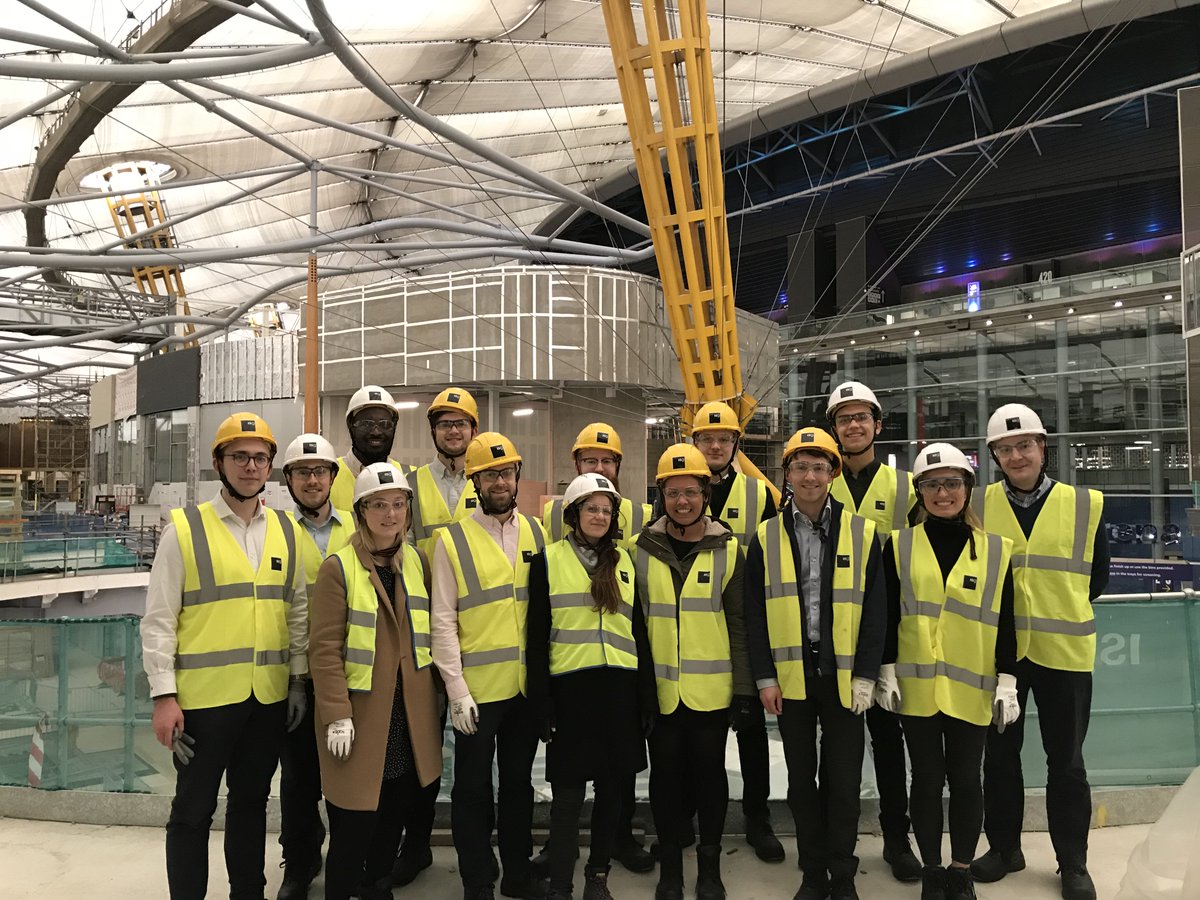 Group of 14 men and women standing in a construction site in high-vis jackets.