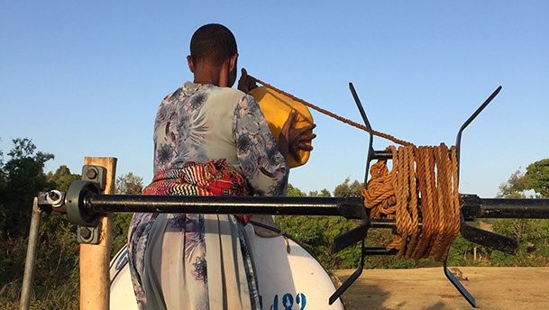 Woman filling water up at a well using a pully system technology