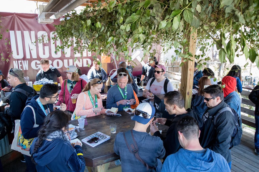 Crowd of event goers at Discovery House eating bbq and drinking drinks around a wooden table
