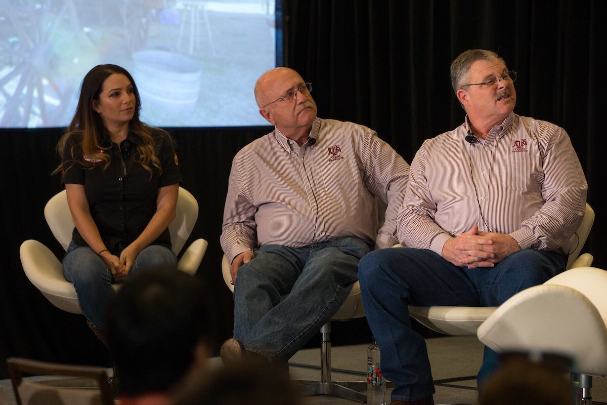 Three hosts sit in chairs on stage