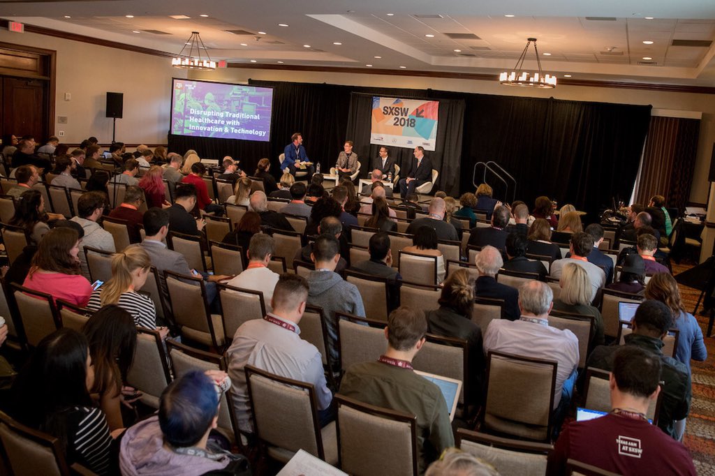Full crowd in conference room with presenters on stage at front
