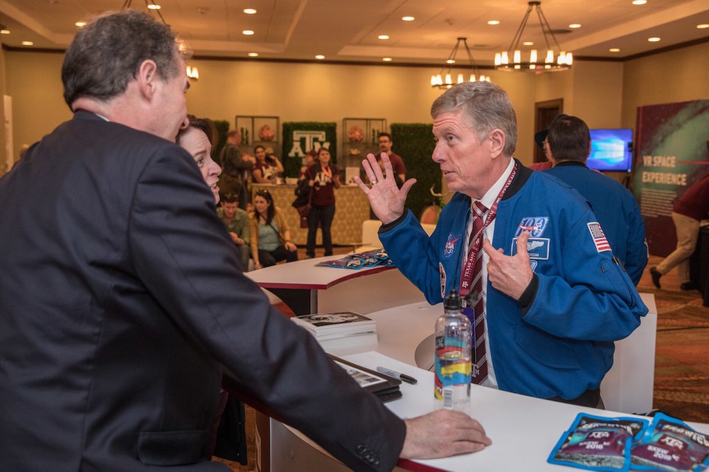 Astronaut wearing NASA jackets talking to two guests in lounge