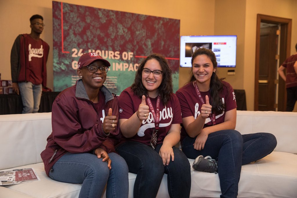 Three Aggies wearing maroon and gigging ‘em on a white couch in lounge