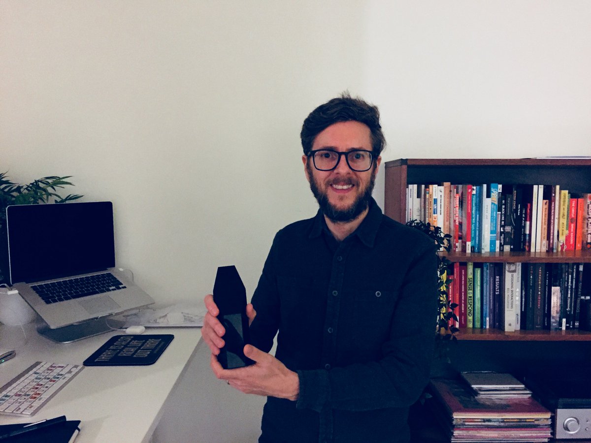 Dean stood in his office holding the Aquent UX design award for 2018.