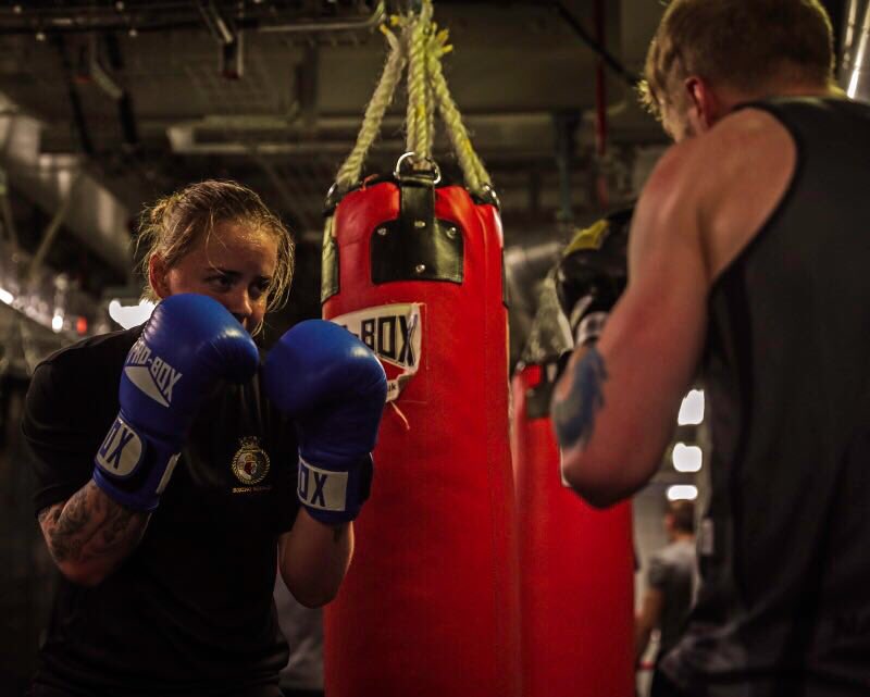 A boxer with gloves up at her face gets ready to punch her opponent in a training session.