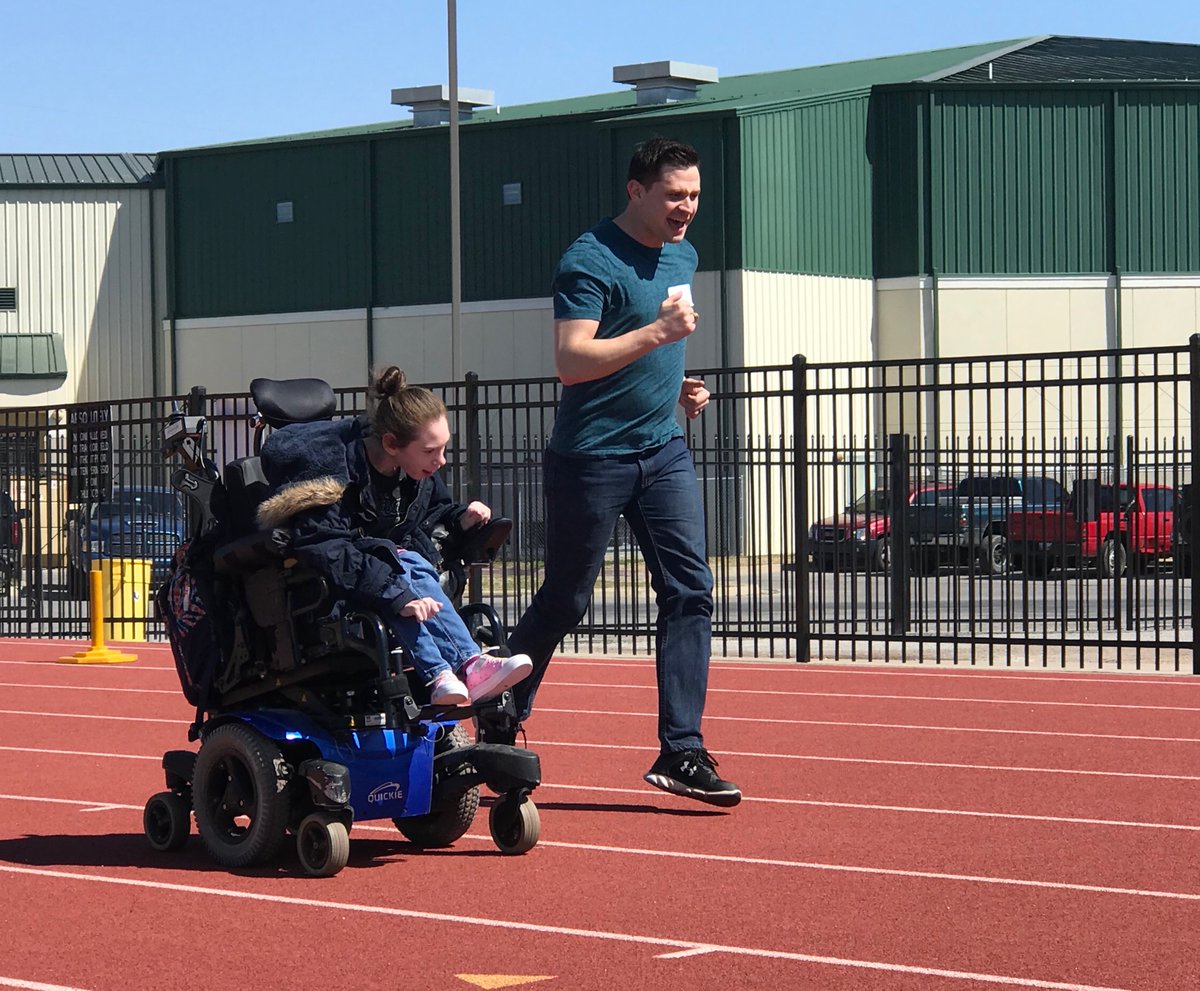 Man running next to a young girl racing in a wheelchair on a track