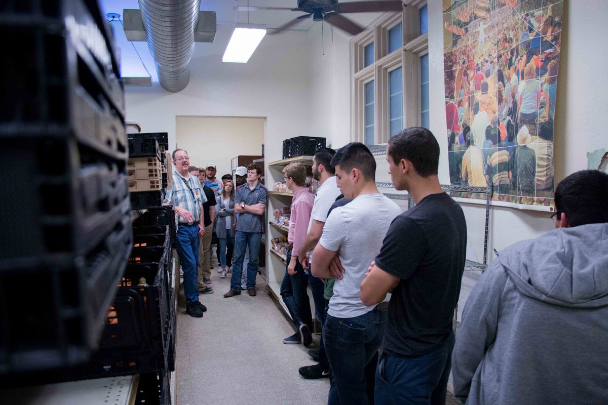 several students listening to a worker at the food bank talk in a storage room
