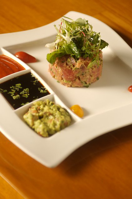 A favorite, our Ahi Tuna Tartare. Hand cut spicy tuna, mayo, avocado relish, truffle oil. Served with soy sauce, Sriracha and herb greens